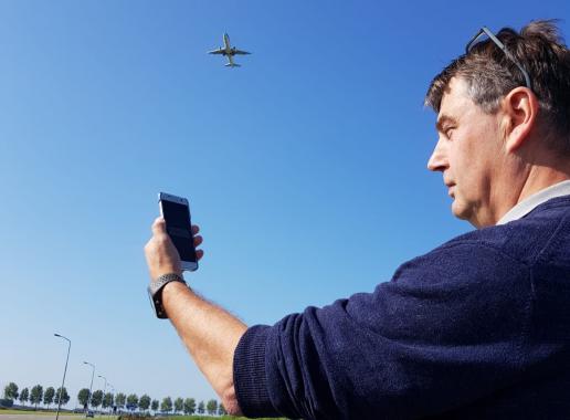 Man met mobiel meet vliegtuiggeluid